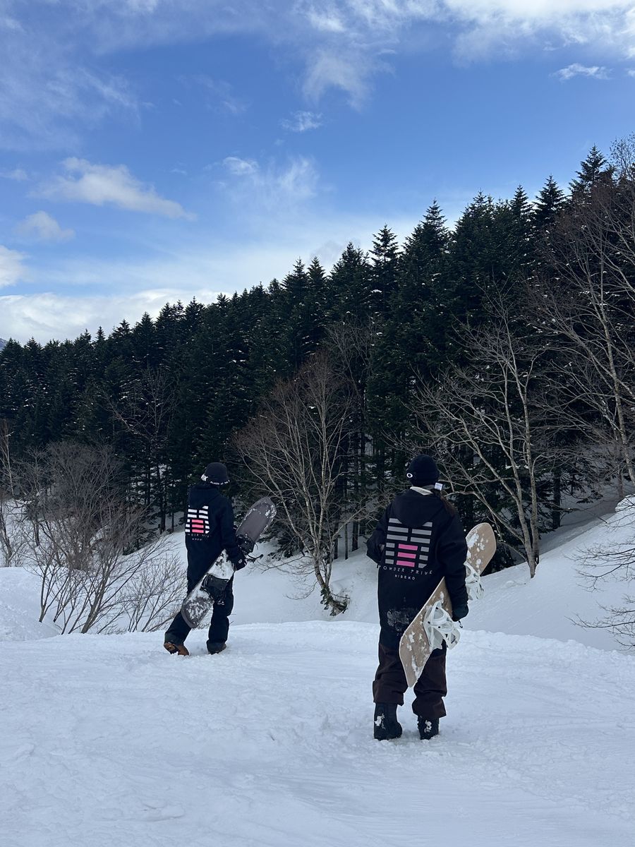 Two riders walking towards the trees with their boards