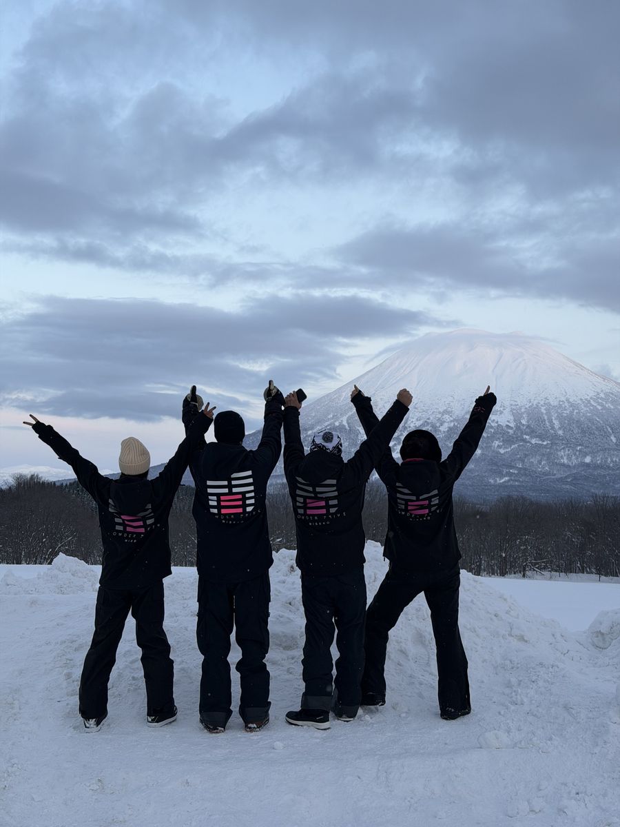 Four riders in Powder Privé hoodies in front of Mount Yōtei