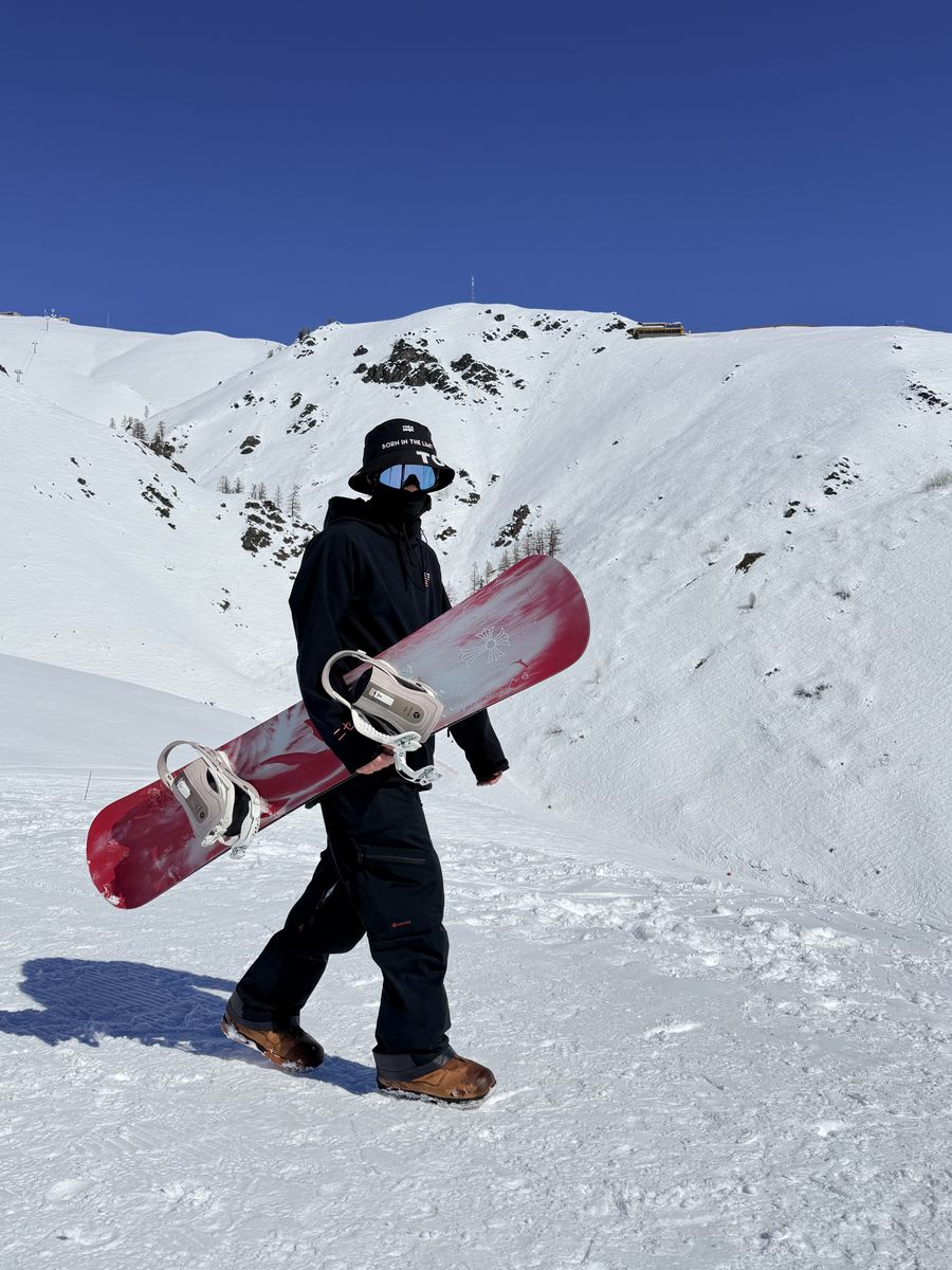 A rider in a Powder Privé hoodie carrying a red snowboard